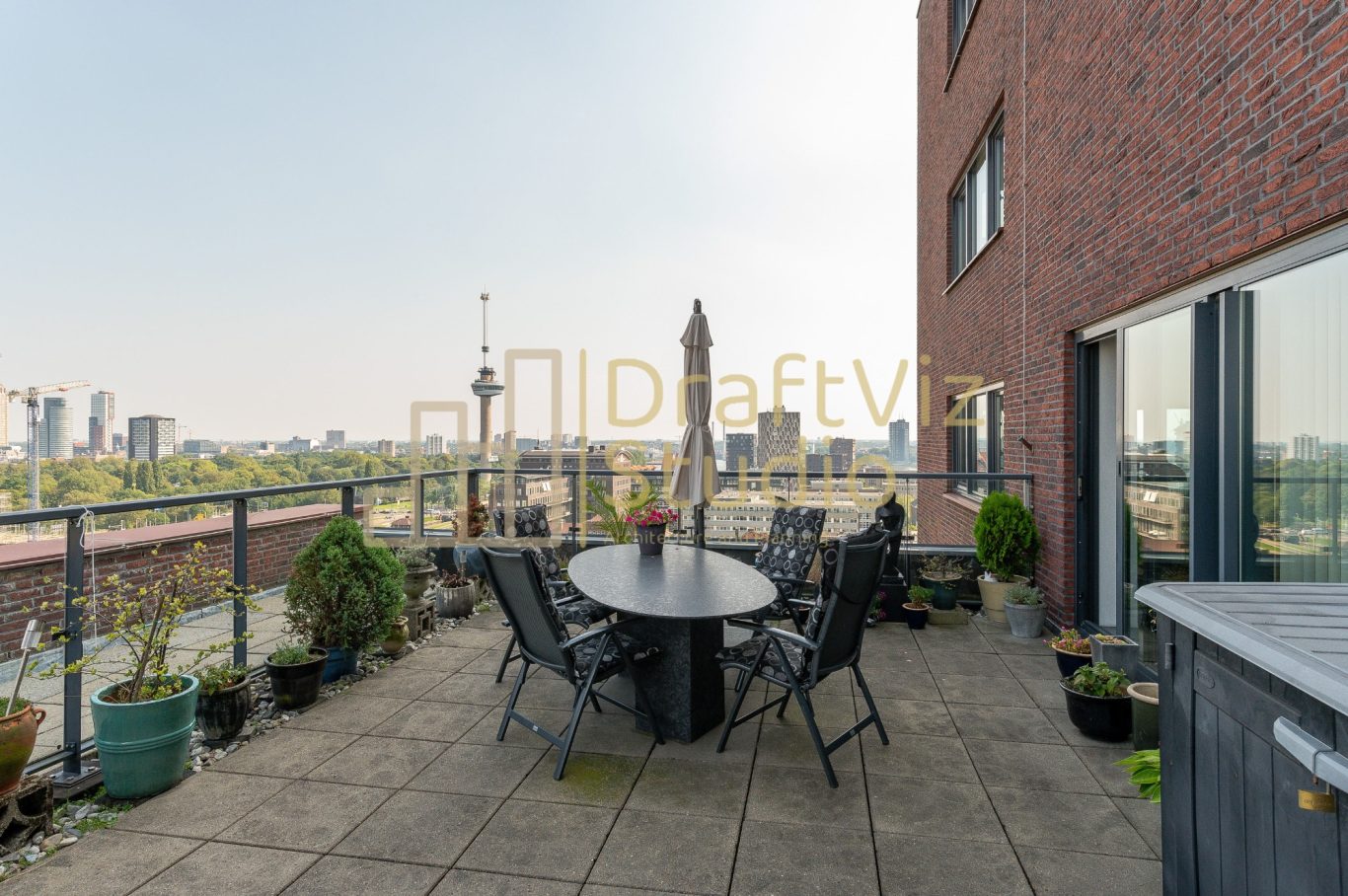 Terrace-Original Image A balcony with a circular table, chairs, and potted plants overlooking the city skyline.